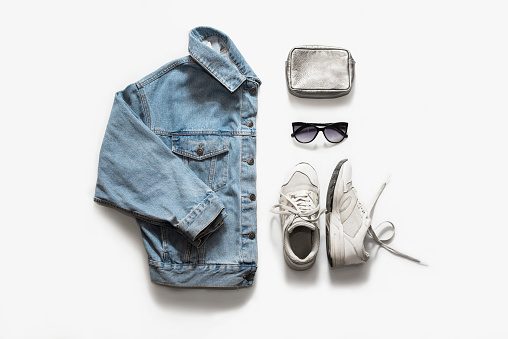 Casual fashion clothes and accessory set on white background. Jean jacket, sneakers, sunglasses, bag. Flat lay, top view.