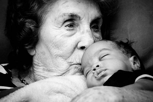 Great Grandma holding a Baby Boy Elderly caucasian Great Grandma posing with her bi-racial white and african american grandson.  The baby is sleeping and the grandma is looking thoughtfully into the mid distance while gently kissing the baby's head as he sleeps. grandma portrait stock pictures, royalty-free photos & images