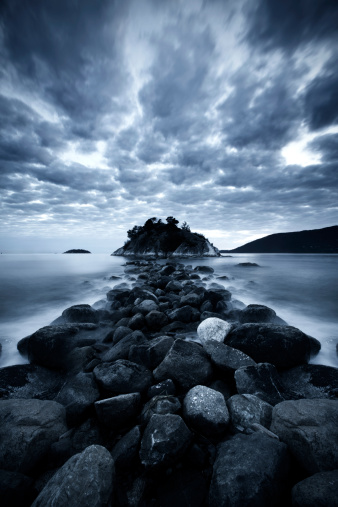 Rocky path out to a dark island under a moody sky.
