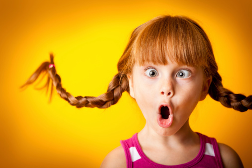 Color photo of a silly, red-haired girl with upward braids making a crazy face!