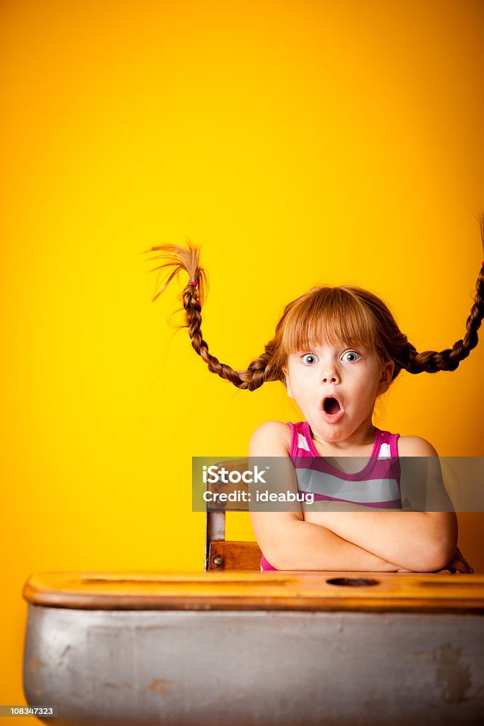 Потрясен Маленькая девочка с вверх Plaits, сидящая в школе стол - Стоковые фото Ребёнок роялти-фри