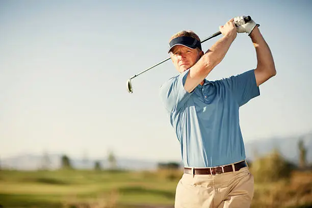 A middle-aged golfer swinging for the green. Just add type for the perfect golfing image.