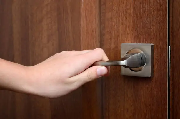 A hand opens the door, holding the doorknob.