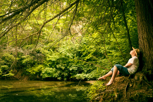 young boy fishing in a pond while leaning on a  big tree - with a retro vintage look