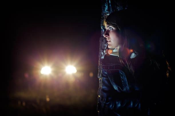 Girl hides in the dark behind a tree from car stock photo