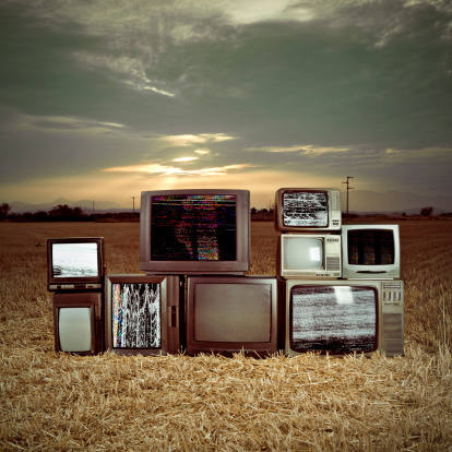 Old televisions in a dark evening field.