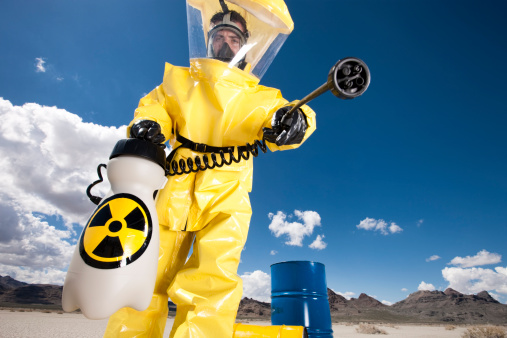 Low angle view of a man dressed in a hazardous materials suit with a chemical sprayer, cleaning up an environmental disaster.
