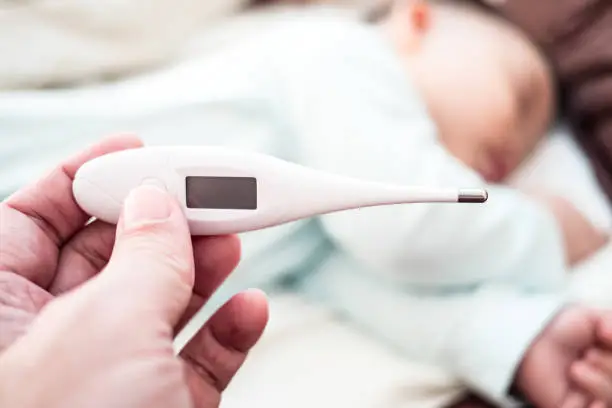 Photo of mother hand hold thermometer with blurred baby background.