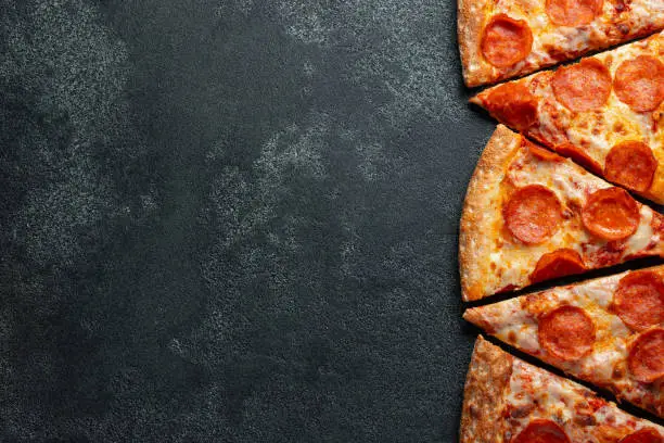 Cut into slices delicious fresh pizza with sausage pepperoni and cheese on a dark background. Top view with copy space for text. Pizza on the black concrete table. flat lay.