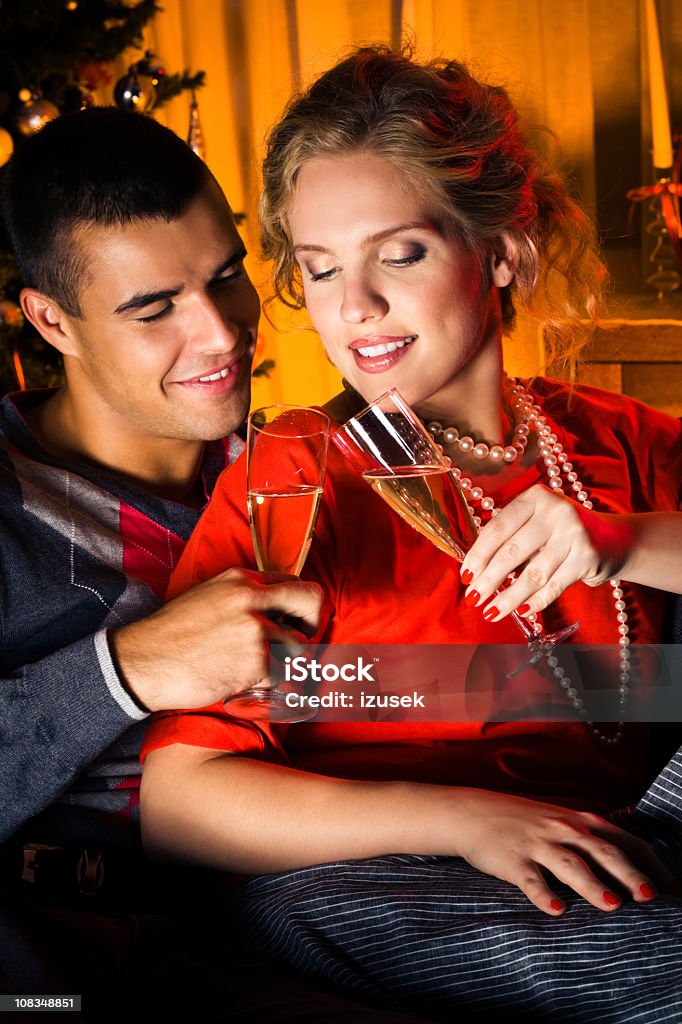 Christmas toast Happy young adult couple celebrating Christmas. They sitting on sofa with champagne glasses and making a toast. Christmas tree in the background. 20-29 Years Stock Photo