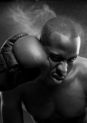 A black and white photo showing an African American boxer taking a blow to the head.