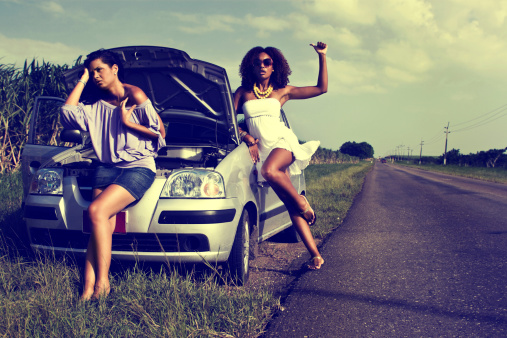 Two women hitchhiking standing beside their car