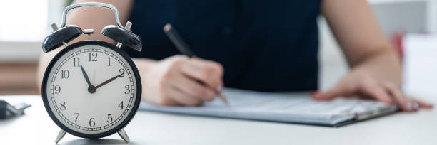 istock Women's hands write in the document. On the table is an alarm clock. 1083495856