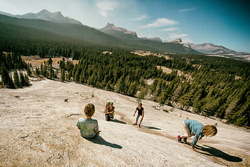 Mother takes her children on a hike in Tuolumne, Yosemite up a dome on an autumn day. Children play and explore on granite in the beautiful mountains.