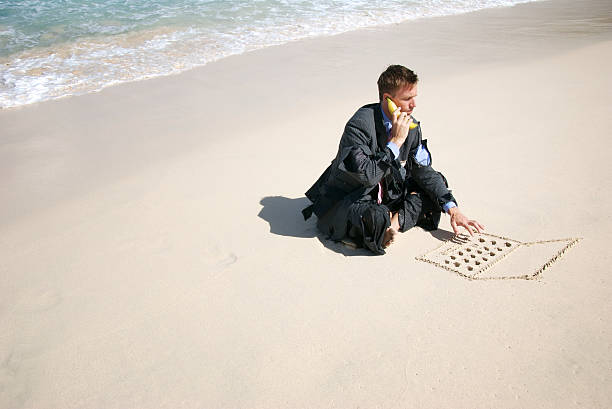 Castaway Businessman Talks w Bananaphone and Types on Sand  castaway stock pictures, royalty-free photos & images