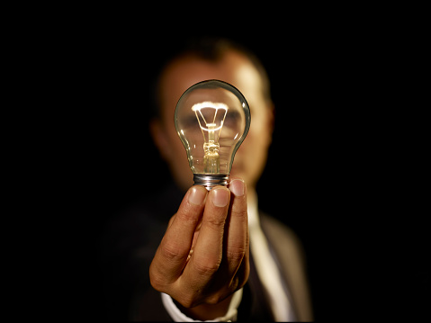 Male businessman holding a lightbulb with power on a black background