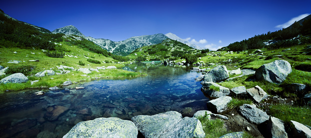 Lake in the Alpine mountains. Beautiful landscape with mountains, green grassy meadows and a hiking trail in springtime.