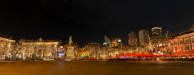 Panoramic night photograph of Plein square in The Hague, Netherlands, illuminated trees and open restaurants.