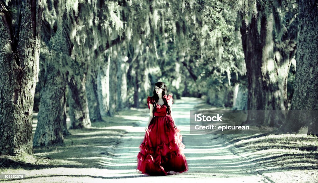 Beautiful woman in red dress walking down white sand road  Dress Stock Photo