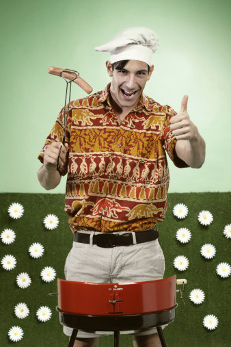 One young man cooking a sausage in a Barbacue. He is wearing a colorful shirt in fiction garden. Format _ Vertical. Concept: Leisure, humor, lifestyle.