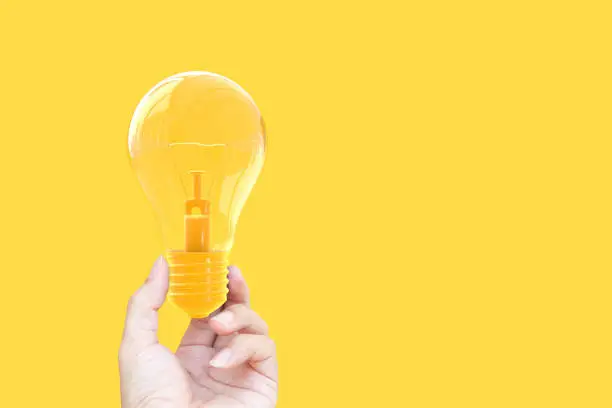 Photo of Hand holding light bulb yellow pastel color