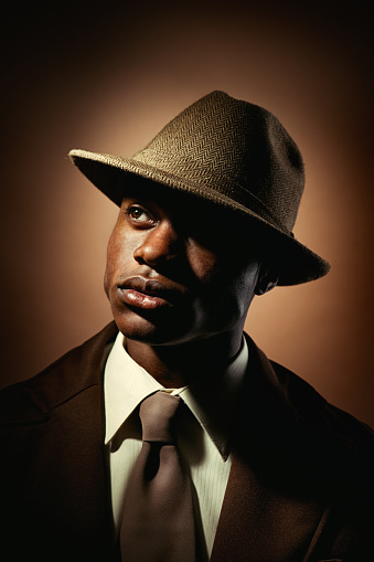 A portrait of a young African American man in 1950s retro style, wearing all brown in front of a brown background.  Dramatic lighting.