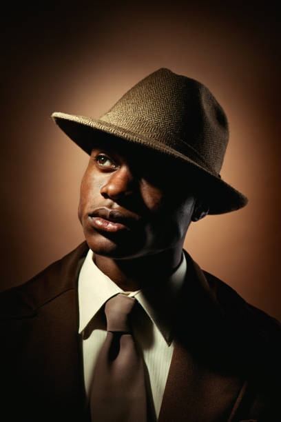 Vintage Mobster Business Man A portrait of a young African American man in 1950s retro style, wearing all brown in front of a brown background.  Dramatic lighting. gangster photos stock pictures, royalty-free photos & images
