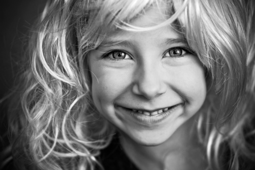 Portrait of a cute female child looking straight at camera and smiling. Monochrome photography concept.