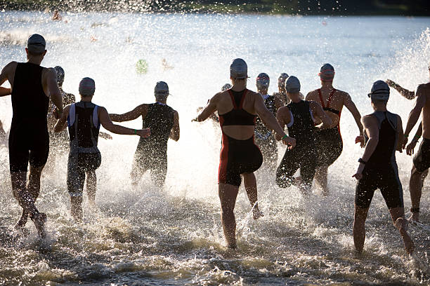 atleti di triathlon all'inizio di triathlon in esecuzione in acqua. - competitive sport competition swimming wetsuit foto e immagini stock