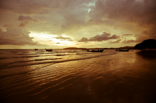 Fishing boats dry on a sandy beach against the backdrop of a sunset over a calm ocean
