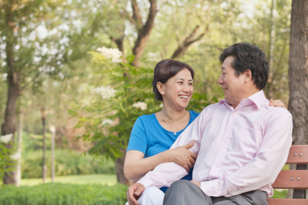 chinese couple sitting on park bench - vacations women men stability imagens e fotografias de stock