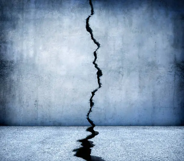 A large crack runs through the middle of a concrete floor and wall.