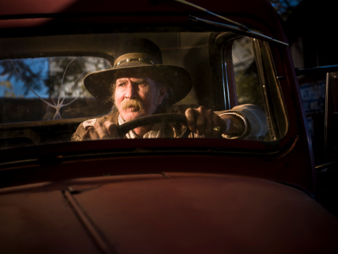 Western man sitting in cab of truck at sunset