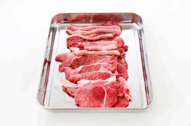 Raw lamb meat on a stainless steel tray on white background.