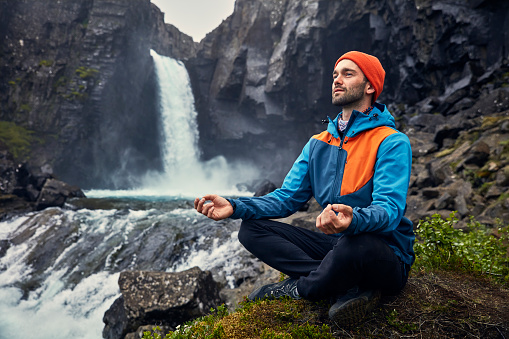 Man meditating in lotus pose near waterfall