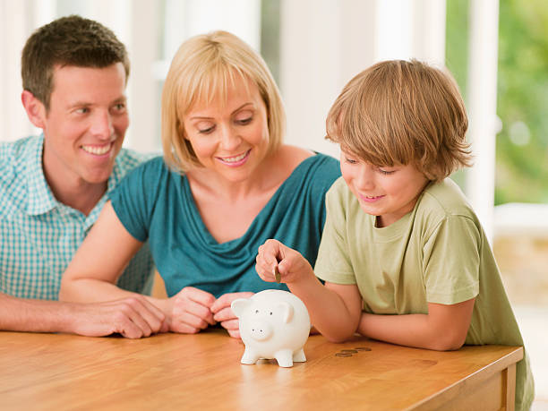 genitori guardando il figlio mettere moneta nel salvadanaio a porcellino - protection finance family wealth foto e immagini stock