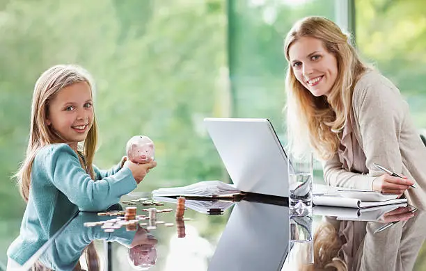 Photo of Mother watching daughter count coins from piggy bank