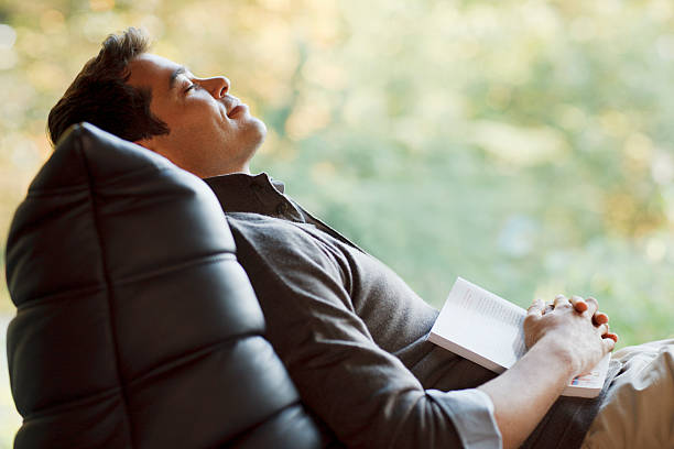 Man napping in chair with book  man sleeping chair stock pictures, royalty-free photos & images