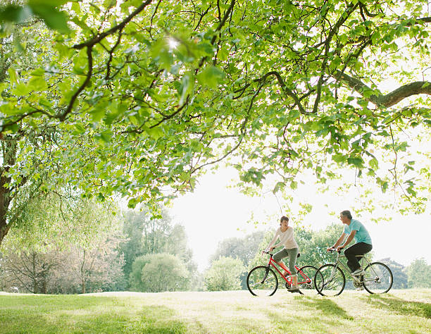 pareja montando una bicicleta debajo de árbol - andar en bicicleta fotografías e imágenes de stock