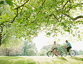 Couple riding bicycles underneath tree