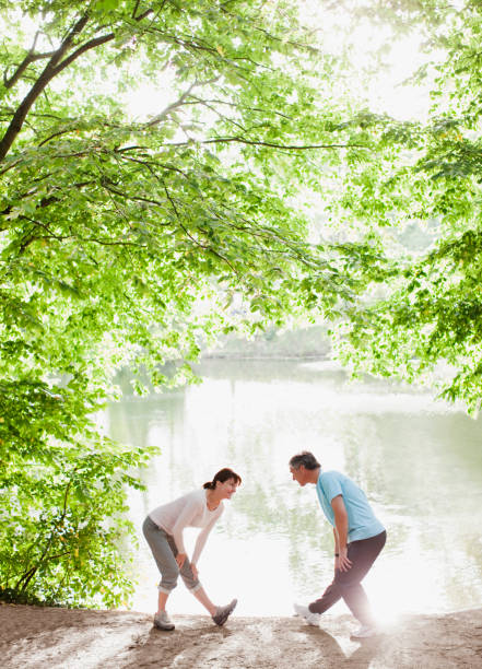 casal de alongamento antes do exercício, perto do lago - couple stretching running jogging - fotografias e filmes do acervo