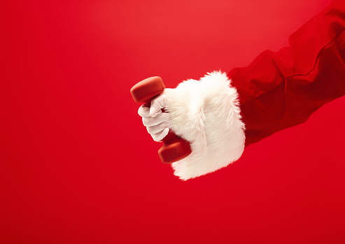 Holidays and celebrations, New year, Christmas, sports, bodybuilding, healthy lifestyle - Santa Claus with dumbbells. Isolated on red background.