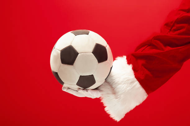 Santa Claus holding a football ball isolated on red background Santa Claus holding a football ball isolated on red studio background evening ball stock pictures, royalty-free photos & images