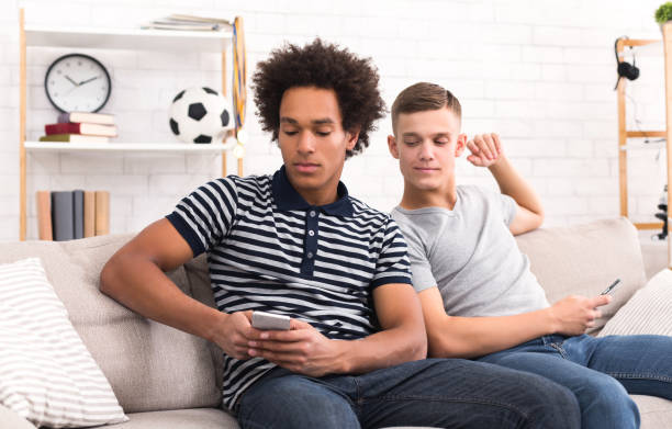 Teenager spying at friends phone at home Teenager spying at his friend texting in phone sitting on couch in living room at home divergent movie review stock pictures, royalty-free photos & images