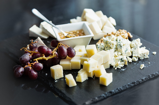 Restaurant cheese plate with sauce. Various types of cheeses with grape on black slate stone. Close up image with selective focus.