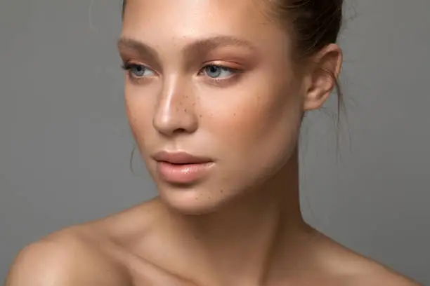 Closeup studio shot of a beautiful young woman with freckles skin posing against a grey background