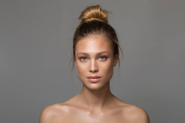 Serene beauty Closeup studio shot of a beautiful young woman with freckles skin posing against a grey background hair bun stock pictures, royalty-free photos & images