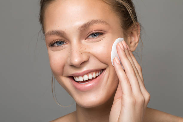 Serene beauty Closeup studio shot of a beautiful young woman with freckles skin, cleansing her face with cotton pad. Posing against a grey background facial cleanser stock pictures, royalty-free photos & images