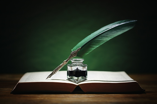 Quill pen and inkwell resting on an old book with green background concept for literature, writing, author and history