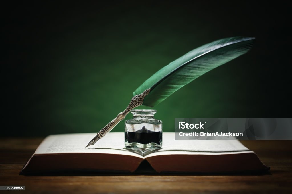 Quill pen and inkwell on old book Quill pen and inkwell resting on an old book with green background concept for literature, writing, author and history Writing - Activity Stock Photo